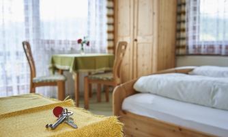 A cozy room with a double bed and a table. On a yellow table runner, there are keys with a red tag.