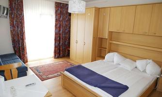 A cozy room with a double bed, a sofa, and a table. Bright walls and curtains create a friendly atmosphere.