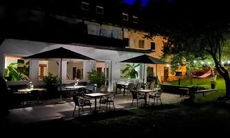 A stylish outdoor area of a restaurant at night, illuminated by soft lights. Tables and chairs under sun umbrellas invite you to linger.