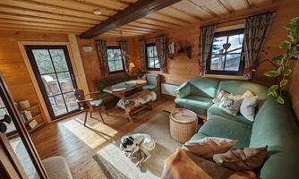 A cozy living space with wooden walls and windows. The decor consists of a green couch, a table, and rustic decorations.