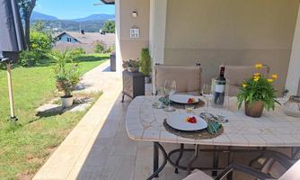 A beautifully set table on a terrace with a view of a green landscape. Flowers and a bottle of wine complete the inviting atmosphere.