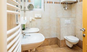A modern bathroom with two sinks and a toilet. The tiles are in neutral colors, and the space feels clean and inviting.