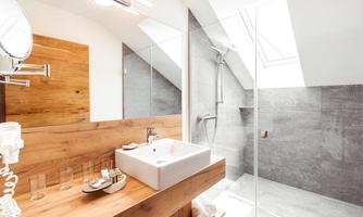 A modern bathroom with wood and stone accents. There is a sink, a shower, and plenty of natural light.