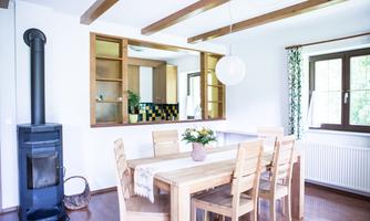 A bright dining room with a large wooden table and chairs. The room has a cozy atmosphere and is equipped with an oven and an open kitchen.