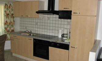 A modern kitchen with wooden cabinets and a stove. On the countertop, there is a coffee machine and other kitchen utensils.