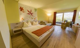 A modern hotel room with a large bed and colorful flowers on the wall. Through the windows, there is a beautiful view of the mountains.