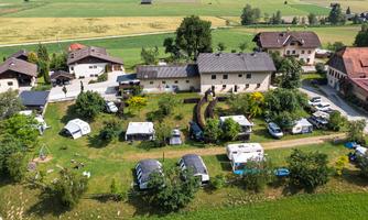 An overview of the campsite with motorhomes and cozy green areas. In the background, rural buildings and a beautiful landscape can be seen.