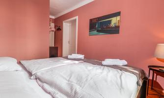 A cozy room with two beds and fresh towels. The wall is painted in a warm pink, and a piece of art hangs above it.