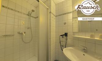 A small, bright bathroom with a shower and a sink. The walls are tiled and there is a mirror above the sink.