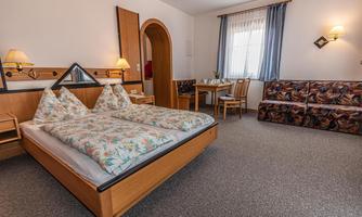 A cozy bedroom with a double bed and a comfortable sofa. The room is bright and inviting, with a table and chairs in the background.