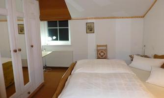 A cozy bedroom with a large bed and a window. There is a wardrobe and a table for work.