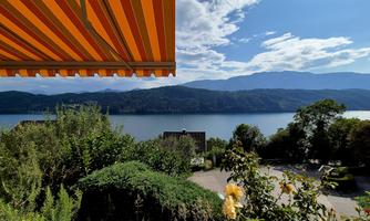 A beautiful view of a lake with mountains in the background. The orange striped awning and the garden plants create an inviting atmosphere.