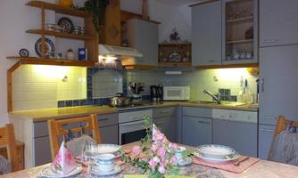 A modern kitchen with wooden shelves and bright walls. The table is beautifully set with dishes and a floral decoration.