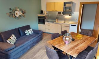 A modern kitchen with a dining area and a cozy living room. The space is bright and inviting with a blue sofa and a wooden table.
