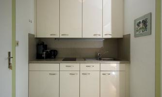A modern kitchen with white high-gloss fronts and a minimalist design. It includes a coffee machine and a kettle, as well as a sink.
