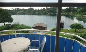 A view of a quiet lake from a balcony. Green meadows and trees surround the water.
