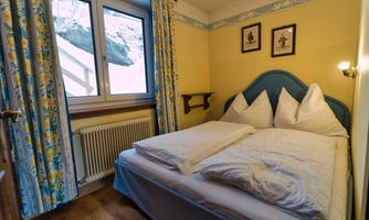 A cozy bedroom with a double bed and colorful curtains. The window offers a view outside and the walls are painted in soft colors.