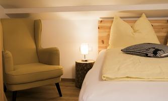 A cozy bedroom with a bed and an armchair. The warm colors and soft light create an inviting atmosphere.