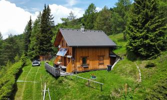 A cozy wooden house surrounded by green forests and meadows. The landscape is calm and invites relaxation.