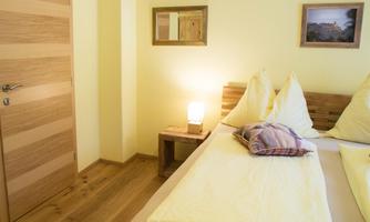 A cozy bedroom with a double bed and yellow bedding. The wall is bright, and there is a window with a nice picture as well as a lamp on the nightstand.