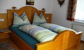 A cozy bedroom with a wooden double bed. The bed covers are decorated with colorful patterns and green colors.