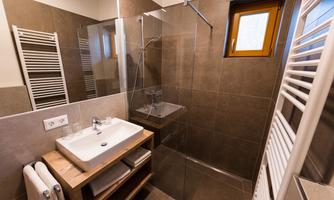A modern bathroom with a glass shower and a sink on a wooden shelf. The walls are in a neutral color tone, and a small window lets in daylight.