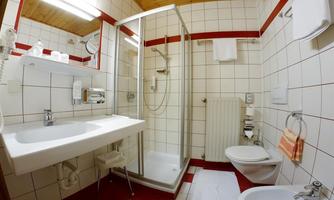 A modern bathroom with a shower, sink, and toilet. The walls are tiled, and there is a bright wooden ceiling.