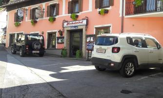 A pink building with shutters that has a restaurant or café entrance. Two cars are parked on the street in front of the house.