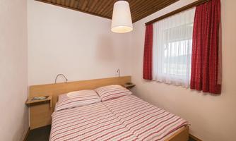 A cozy bedroom with a double bed and a wooden ceiling. Red curtains add a warm accent to the room.