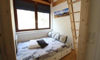 A cozy bedroom with a double bed and large windows. A wooden ladder leads to an attic area.