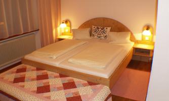 A cozy bedroom with a double bed and soft lighting. The floor is equipped with a colorful carpet.
