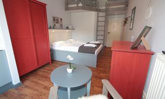 A modern room with a double bed and bunk beds. The room is designed in bright colors and has a small table as well as a red cabinet.