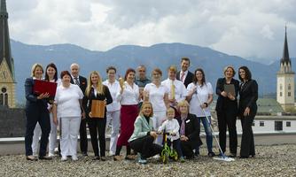 A group of people is standing on a roof with mountains in the background. They are all wearing similar clothing and smiling at the camera.