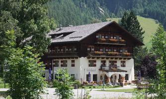 A charming alpine house with balconies, surrounded by trees and green hills. The facade is traditional and inviting, ideal for a stay in nature.