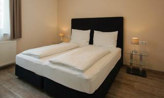 A modern bedroom with a large bed and two pillows. The walls are painted in a neutral tone and there is soft light from the nightstands.