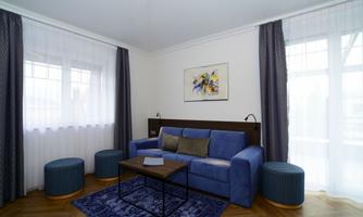A modern living room with a blue sofa and a wooden table. Large windows provide plenty of daylight and a cozy atmosphere.
