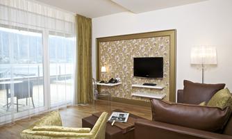 A modern hotel room with a cozy seating area and a television on the wall. Large windows offer a view of the surroundings.