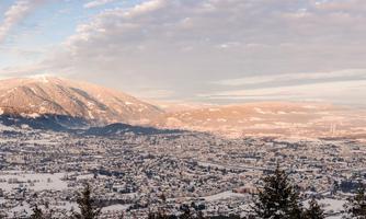 A wintry landscape with snow-covered mountains and a small village in the valley. The sky is bright blue with some clouds.