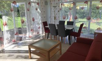 A bright, inviting room with large windows and elegant curtains. The room is furnished with a table, chairs, and a cozy sofa.