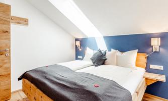 A modern bedroom with two beds and bright furnishings. The walls are designed in blue and white, and the light gently falls on the beds.