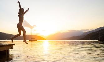 A girl joyfully jumps into the water at sunset. The scene depicts a relaxed atmosphere by the lake.