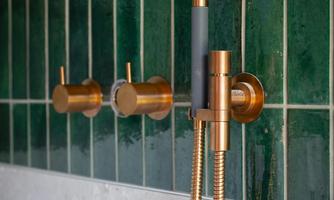 A modern shower set with shiny copper fittings on a green tiled wall. The combination of color tones creates a stylish atmosphere.