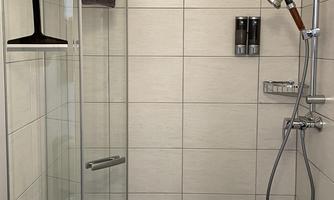 A modern shower with glass doors and bright tiles. On the wall are shampoo dispensers and a towel.