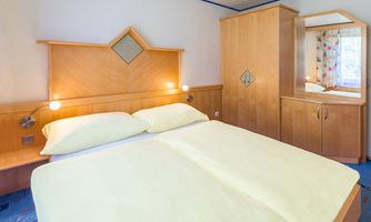 A cozy bedroom with a double bed and bright bed linen. The wooden furniture and the large mirror create an inviting atmosphere.