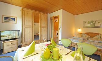 A cozy room with wooden furniture and a dining area. In the background, two beds and a television are visible.