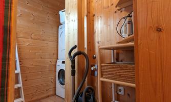 A small room with wood paneling and a washing machine and dryer. On a shelf are household items and a vacuum cleaner is visible.