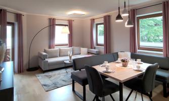 A modern living room with a cozy sofa and a dining table. Large windows let in plenty of light and create a friendly atmosphere.