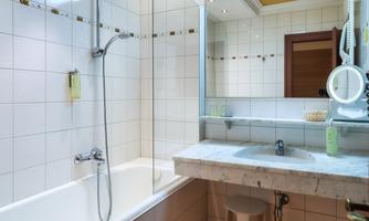 A modern bathroom with a bathtub and a shower. The room is bright and well-organized, with a sink and a mirror.