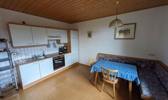 A bright kitchen with white cabinets and a dining area. The table is covered with a blue tablecloth and there is a cozy seating area.