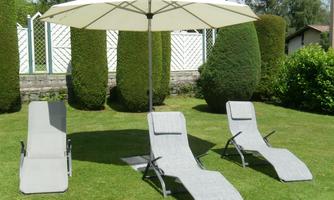 A relaxing seating area in the garden with three lounge chairs and a large sun umbrella. The surroundings are green and well-maintained.
